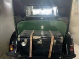 an old black car with luggage on the back