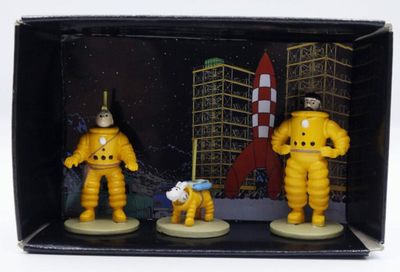 trois figurines d'astronautes dans une boîte, avec une navette spatiale en arrière-plan