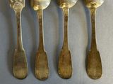 five silver spoons and a fork are lined up on a table