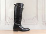 des bottes en cuir noir cloutées sur un parquet, devant un mur blanc