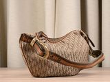 beige and brown handbag sitting on top of a wooden table next to a curtain