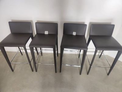 four brown leather bar stools in a row against a white wall