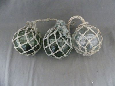 three green glass ornaments hanging from a string on a white cloth