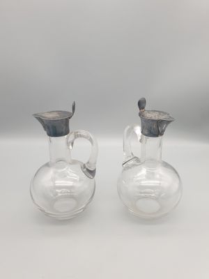 une paire de cruches en verre transparent munies de poignées en métal, posées sur un plan de travail blanc