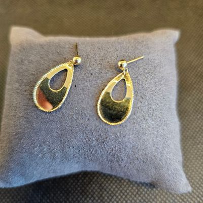 une paire de boucles d'oreilles dorées et noires posées sur un coussin