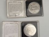 two silver coins are in a box on a white surface