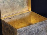 a silver box with a gold lid on a black background