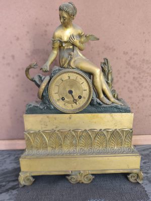 a gold clock with a statue of a woman sitting on top of it