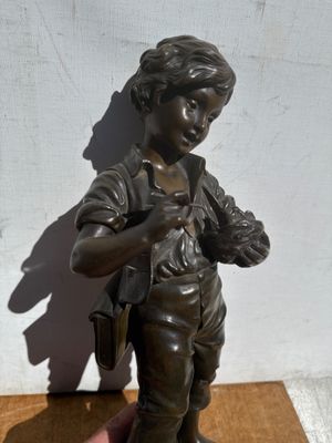 statue en bronze représentant un garçon tenant un oiseau, posée sur un socle en bois