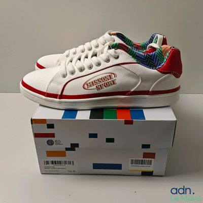 Quelqu'un porte une paire de baskets blanches ornées d'un motif coloré.