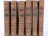 six vieux livres sont alignés sur une surface blanche