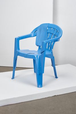 une chaise en plastique bleue posée sur une estrade blanche dans une pièce