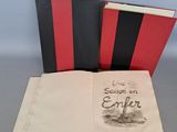 un livre ouvert posé sur une table, à côté d'un livre rouge et noir