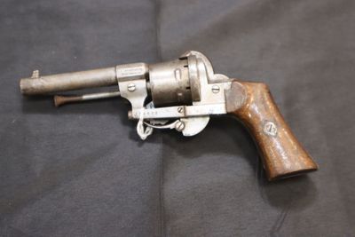 un vieux revolver avec une crosse en bois posé sur un tissu noir