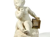 une petite statue représentant un bébé assis sur un oreiller, avec un oiseau dans une cage