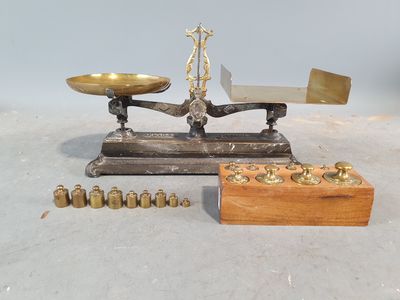 une balance ancienne avec des poids en laiton et un coffret en bois, posée sur une surface blanche