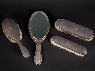 trois brosses à cheveux anciennes et un miroir posés sur un support noir