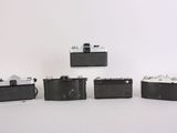 four old cameras are lined up in a row on a white surface
