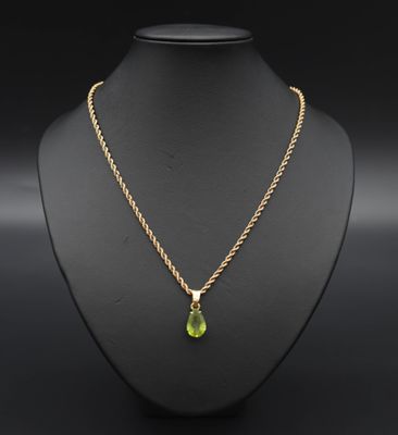 Un collier en or orné d'une pierre verte en forme de larme est suspendu à un mannequin.