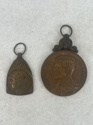 two small bronze medals of a man and a woman on a white surface