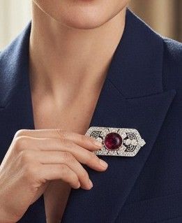 a woman that is wearing a brooch with a red stone
