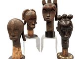 three wooden sculptures of heads on stands on a white surface