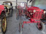 two old tractors in a garage with a man standing next to them