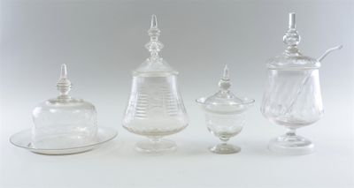 three clear glass containers with lids and a saucer on a white surface