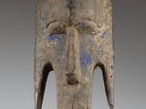 a close up of a wooden mask on a stand on a white surface