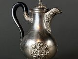 une cafetière ancienne en argent avec une poignée noire sur fond gris