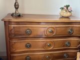 a dresser with a lamp on top of it next to a bed