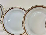 several white plates with gold trims are lined up on a white surface