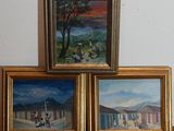 trois tableaux encadrés représentant une scène de village, posés sur une table en bois