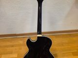 a black acoustic guitar sitting on top of a hard wood floor