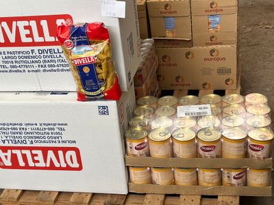 Plusieurs cartons de conserves sont empilés sur des palettes dans un entrepôt