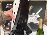 quelqu'un tient une maquette Lego représentant une navette spatiale devant une bouteille de champagne
