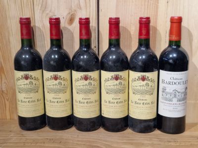 six bottles of red wine lined up on a wooden shelf
