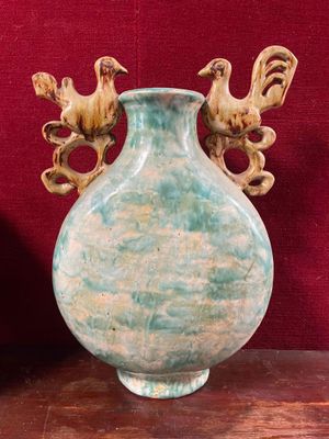 a green vase with two birds on it on a table
