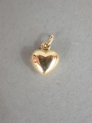 un gros plan d'un pendentif en forme de cœur doré posé sur une surface blanche
