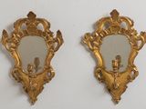 une paire de miroirs dorés richement décorés accrochés à un mur blanc, avec un candélabre