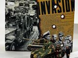 toy soldiers are standing next to a toy tank in front of a book