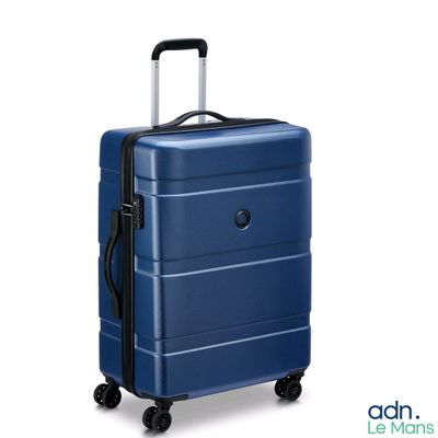 La valise bleue repose sur ses roulettes, posée sur une surface blanche.