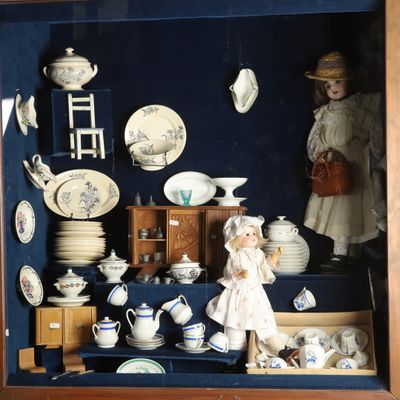 une vitrine contenant une poupée et remplie de porcelaine