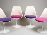 quatre chaises « Tulip » avec des coussins violets, alignées sur une surface blanche