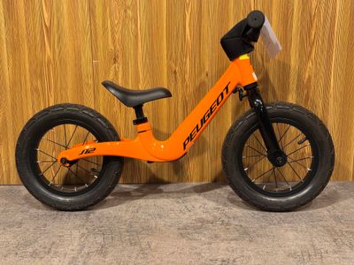 un vélo d'équilibre orange adossé à un mur en bois, devant un mur en bois