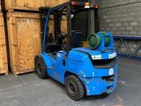 un chariot élévateur bleu garé devant une pile de caisses en bois
