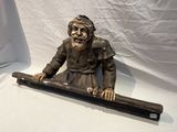 une statue représentant un homme assis sur une longue planche de bois