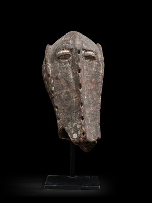 un masque en bois posé sur un socle, sur fond noir