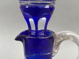 a blue glass pitcher with a silver handle on a table
