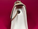 a white purse with a chain on it on a pink surface